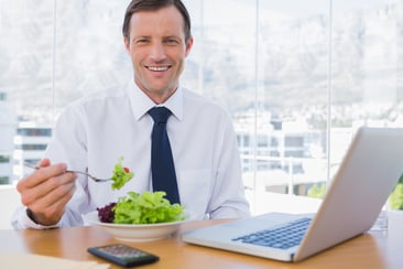Happy businessman eating a salad on his desk during the lunch time